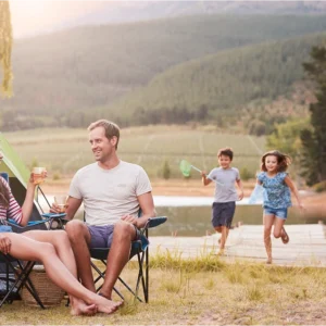 Family camping by a lake, children running.