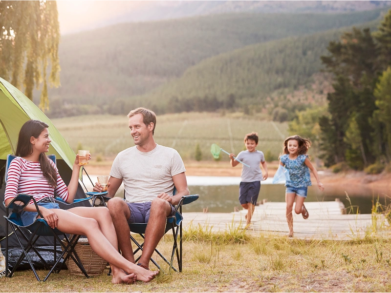 Family camping by a lake, children running.