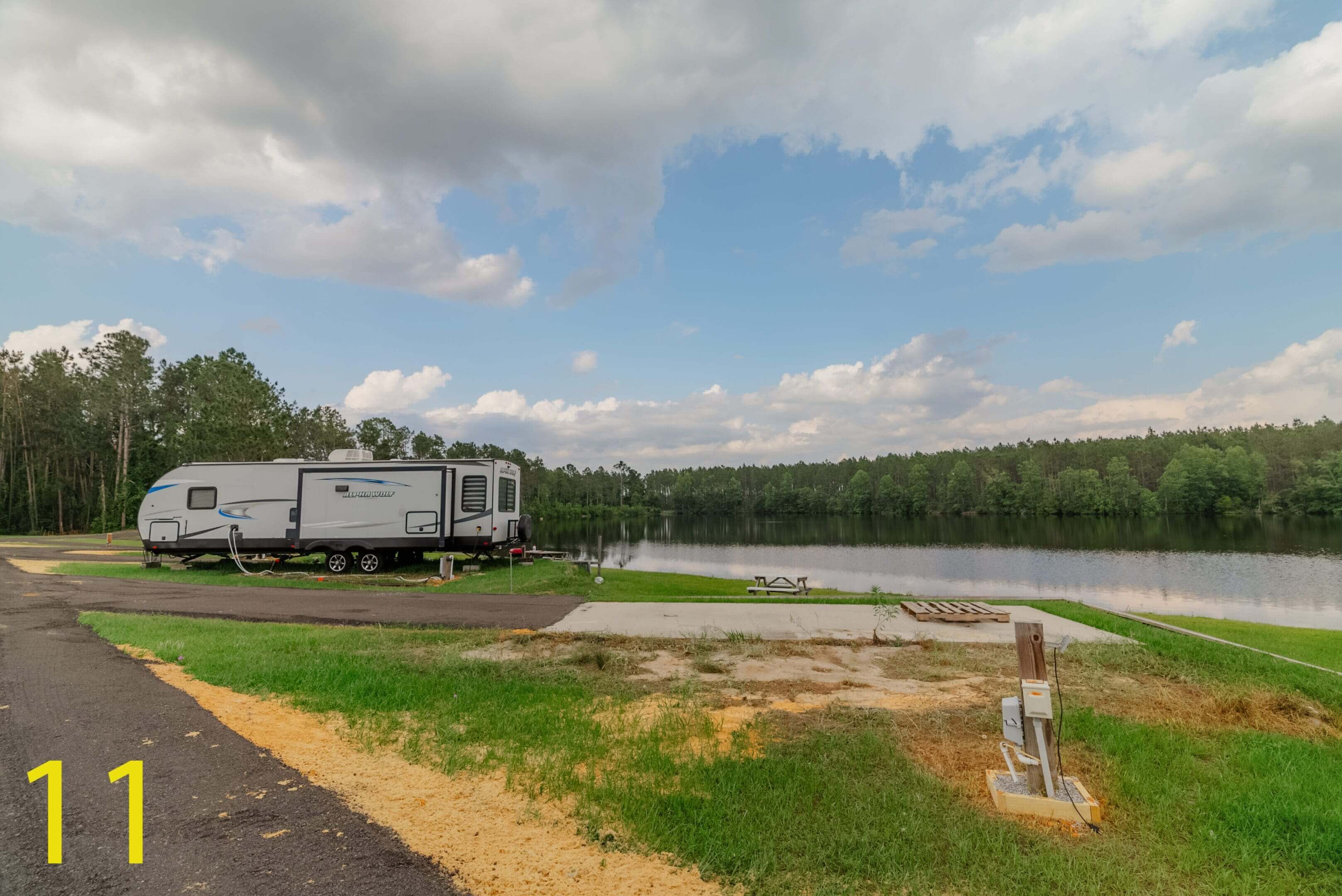 A camper parked near a lake under a blue sky with clouds.