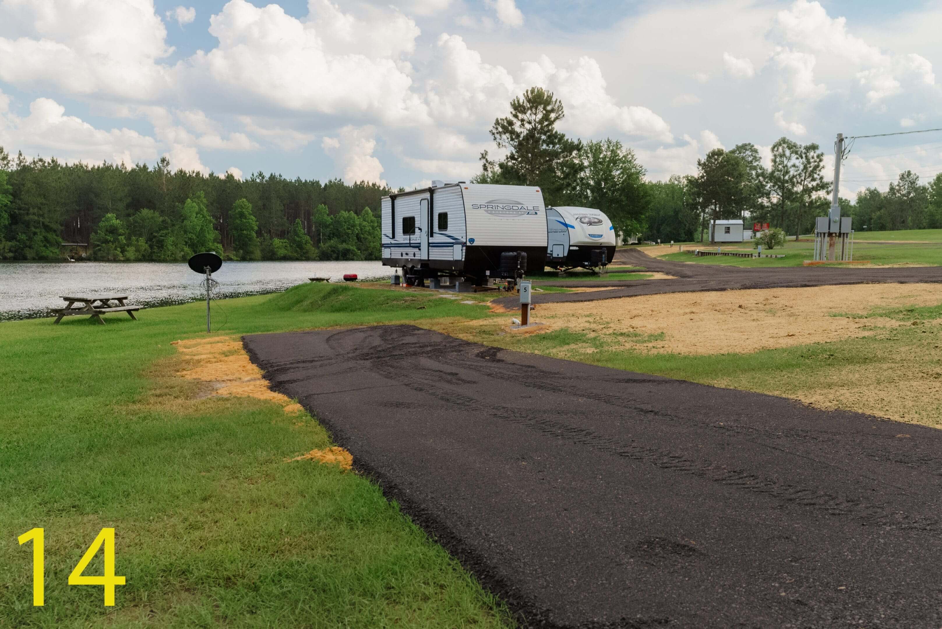 A camper trailer parked on a grassy campground with trees in the background.