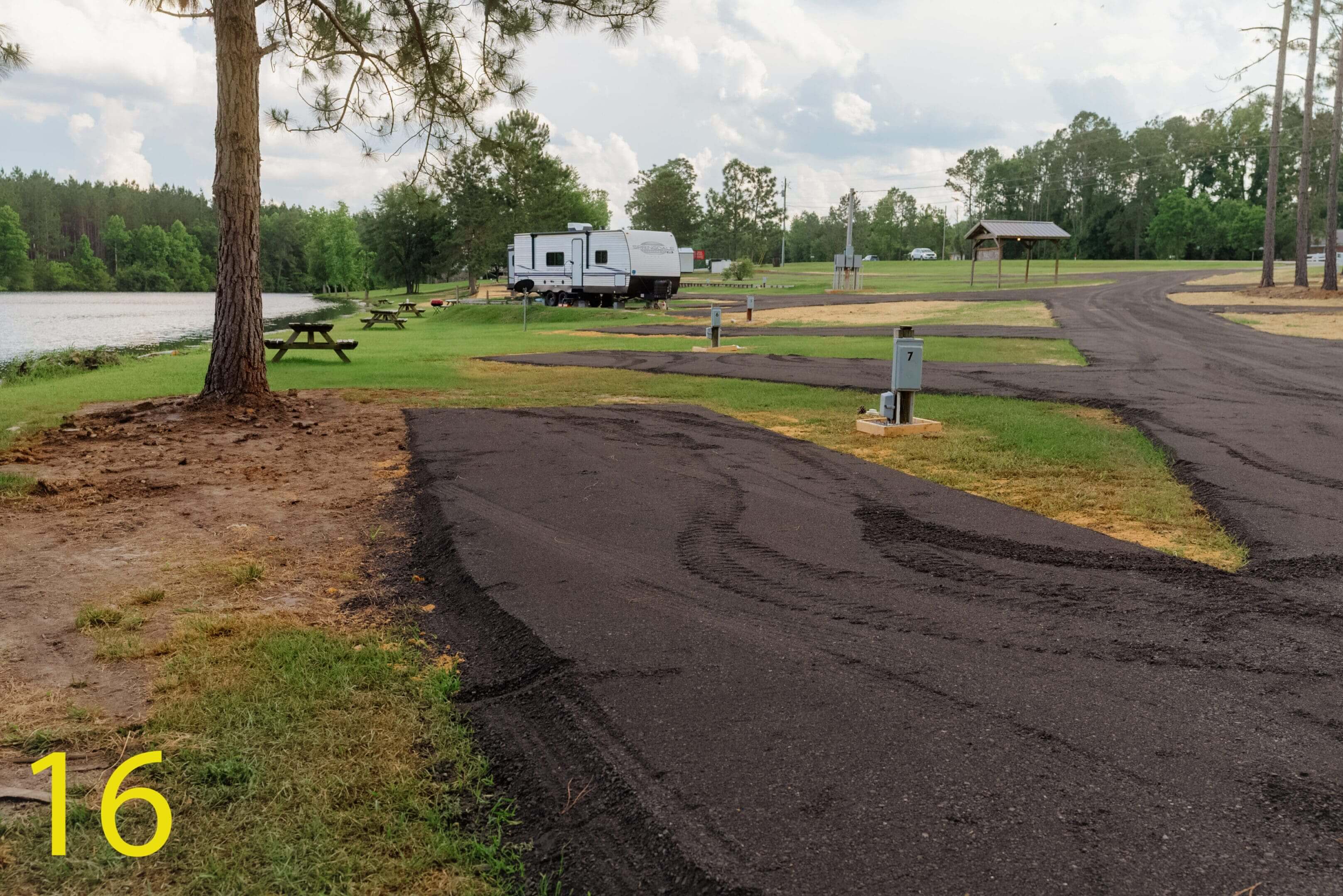 An empty paved campsite with an RV in the distance under a cloudy sky.