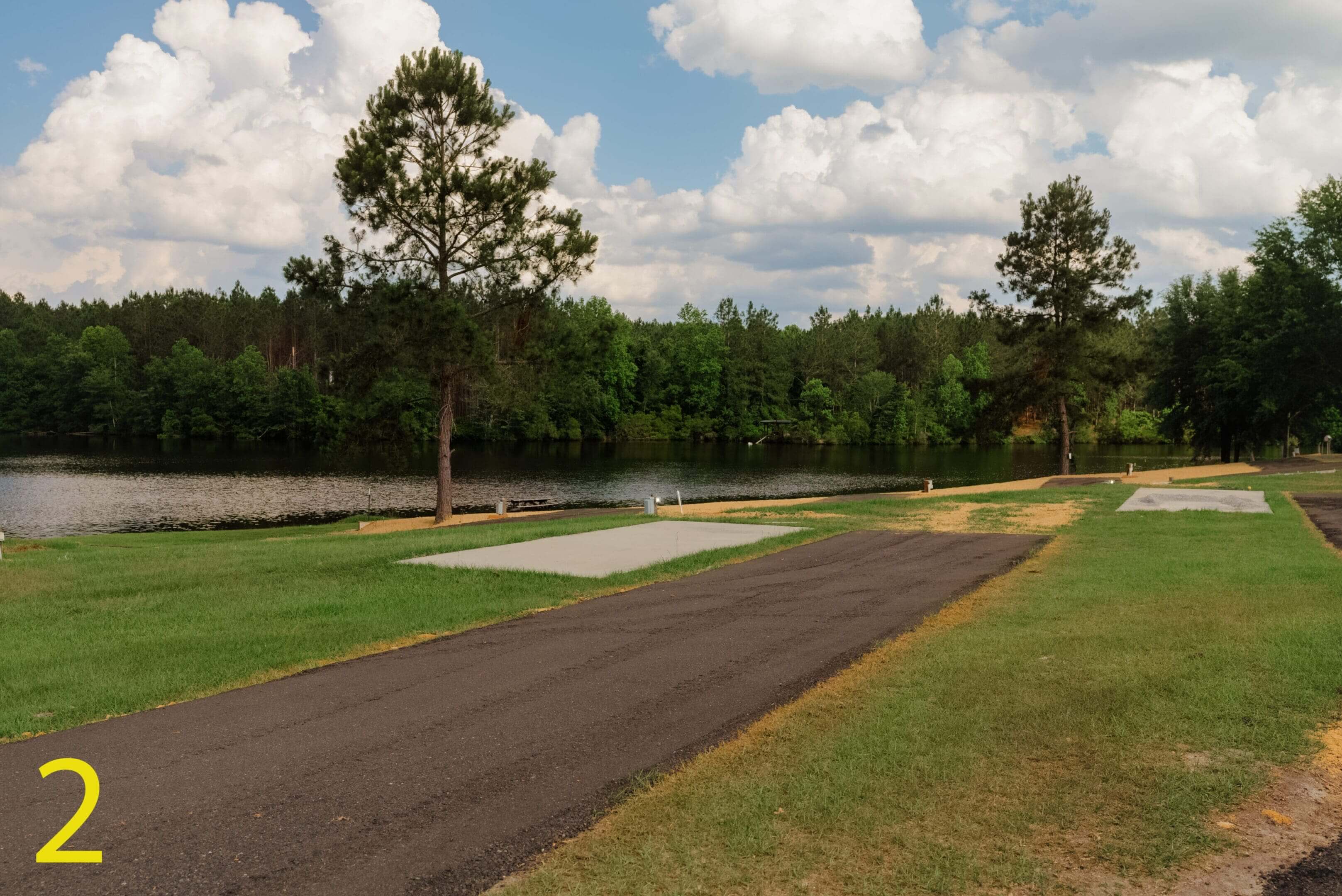 A paved path beside a small pond with trees and a cloudy sky.