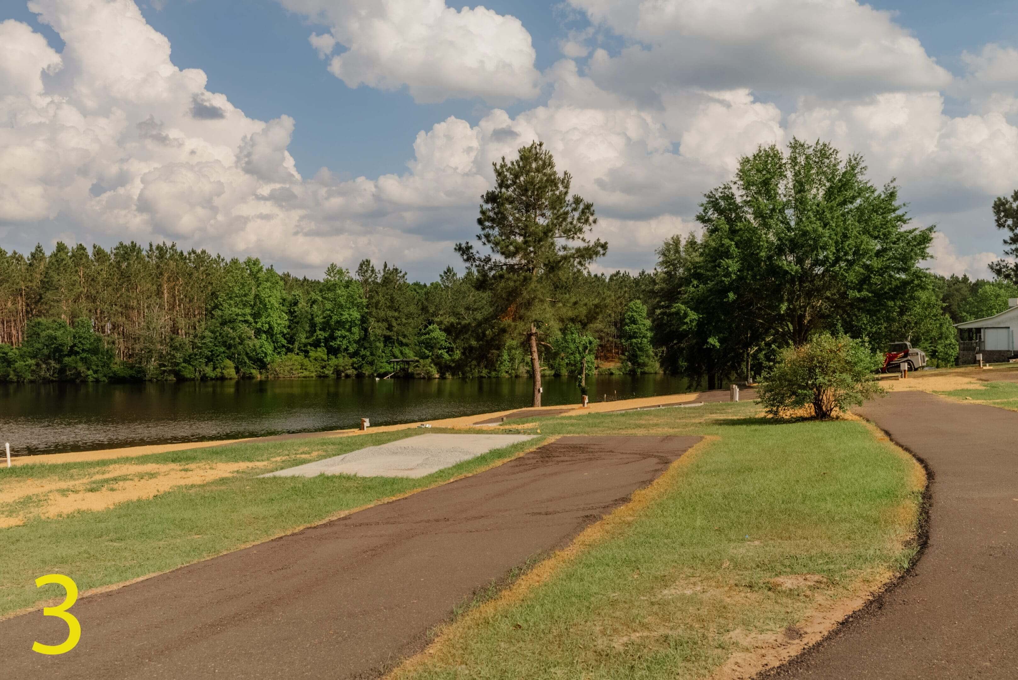 A paved path beside a calm lake with trees and clouds.