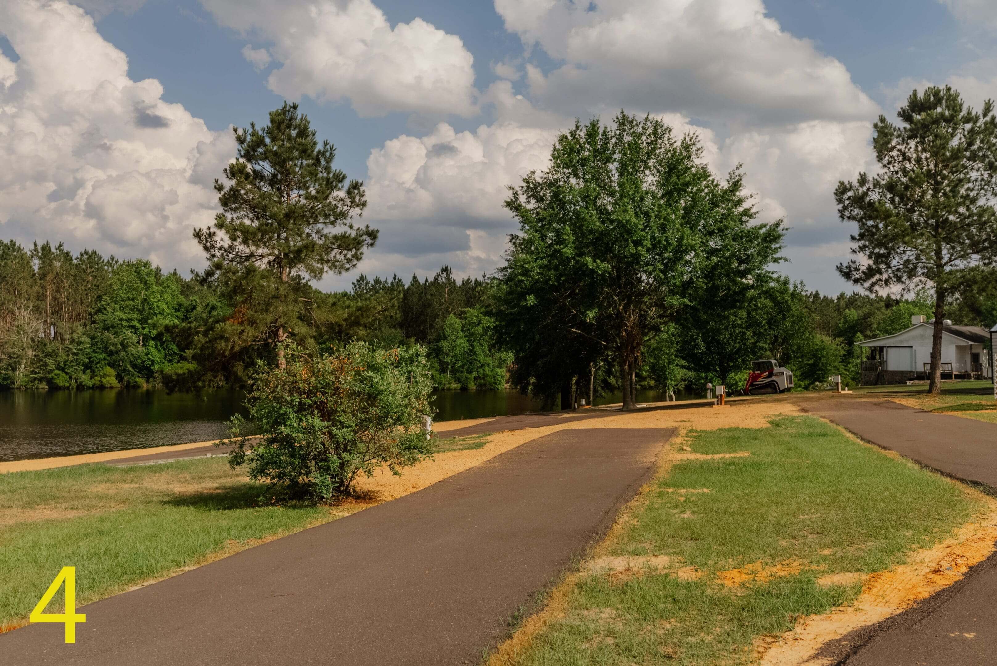 A paved pathway curves through a park with green trees and a partly cloudy sky.