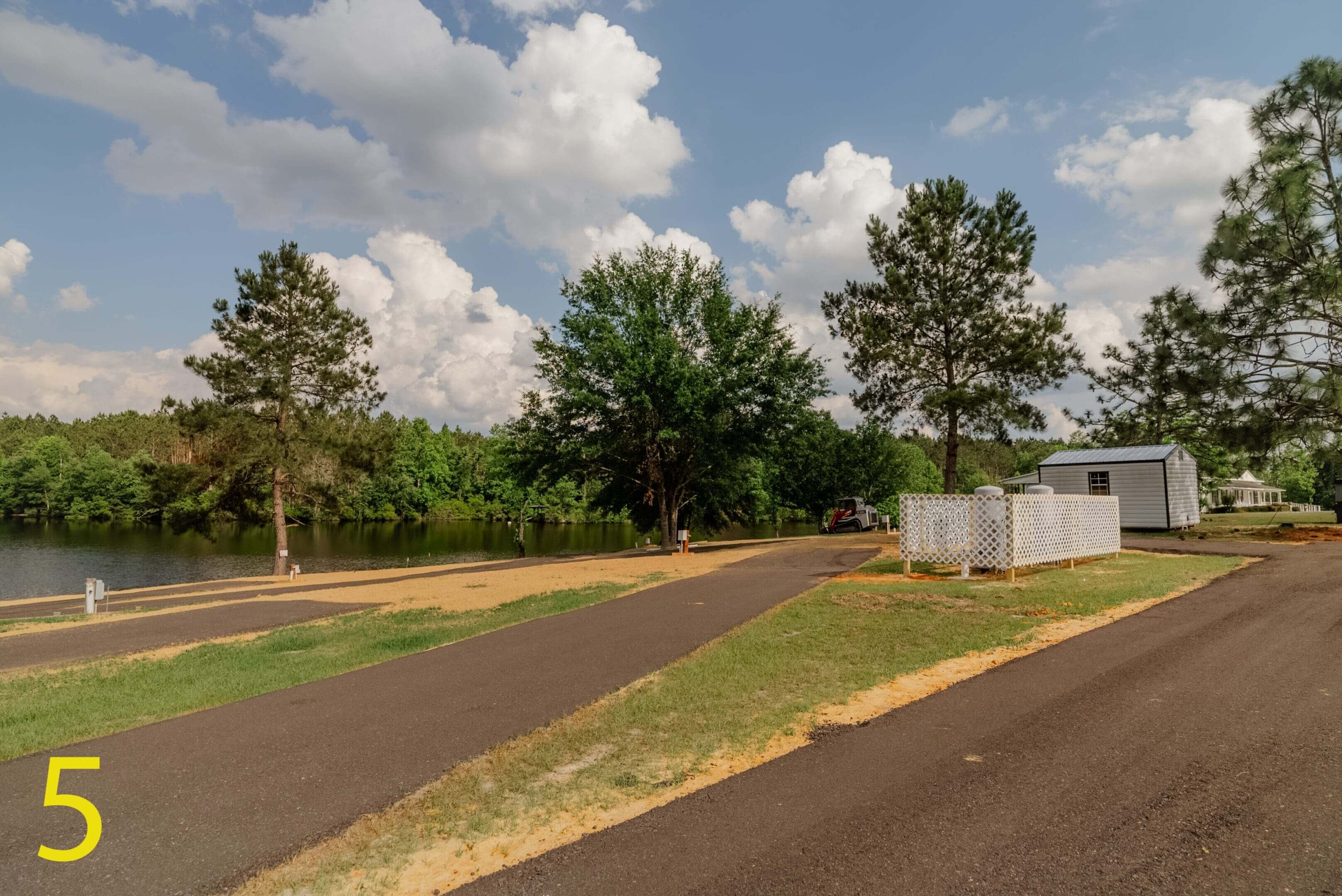 A paved road beside green trees under a partly cloudy sky.