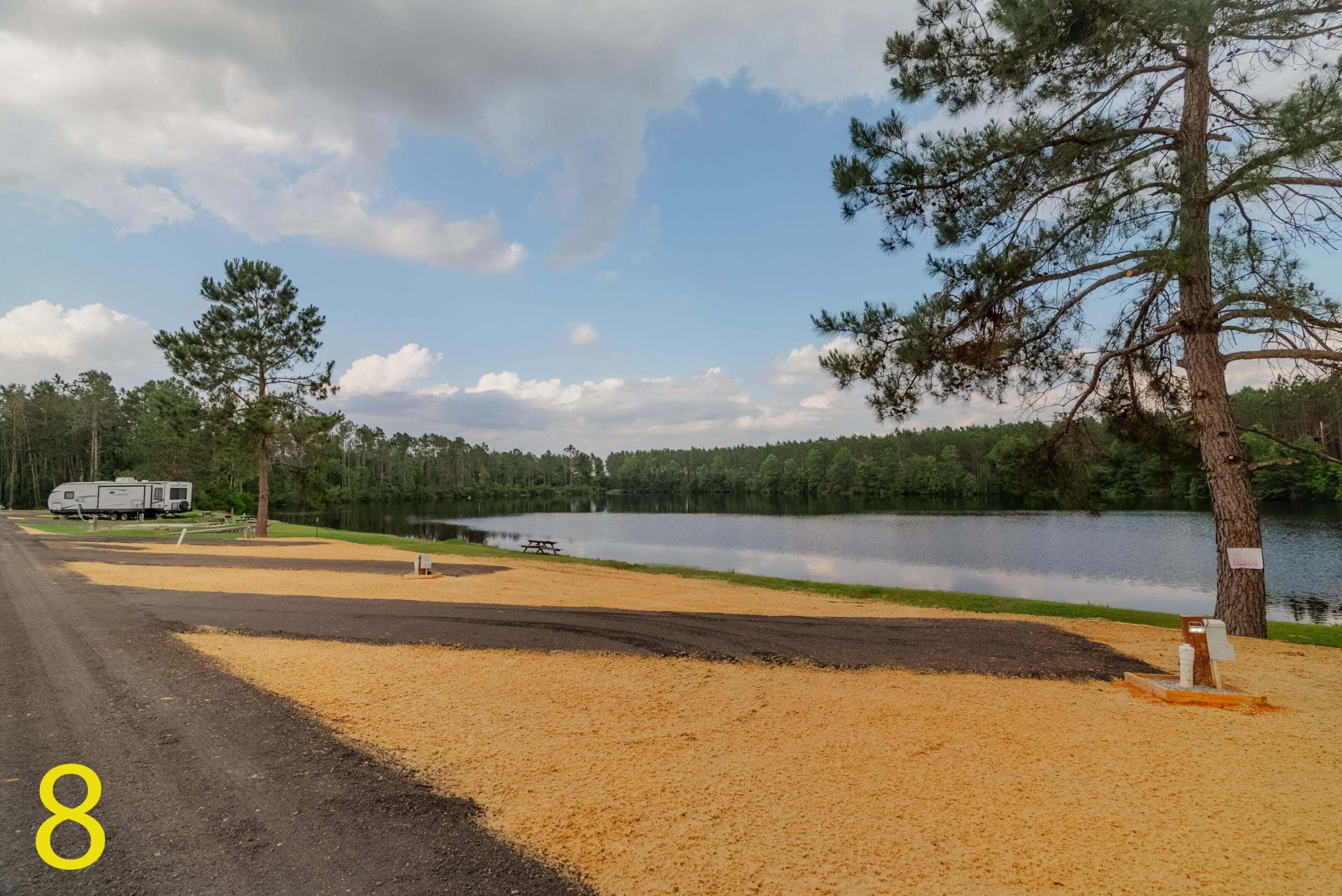 A tranquil lake with sandy shore and trees under a partly cloudy sky.