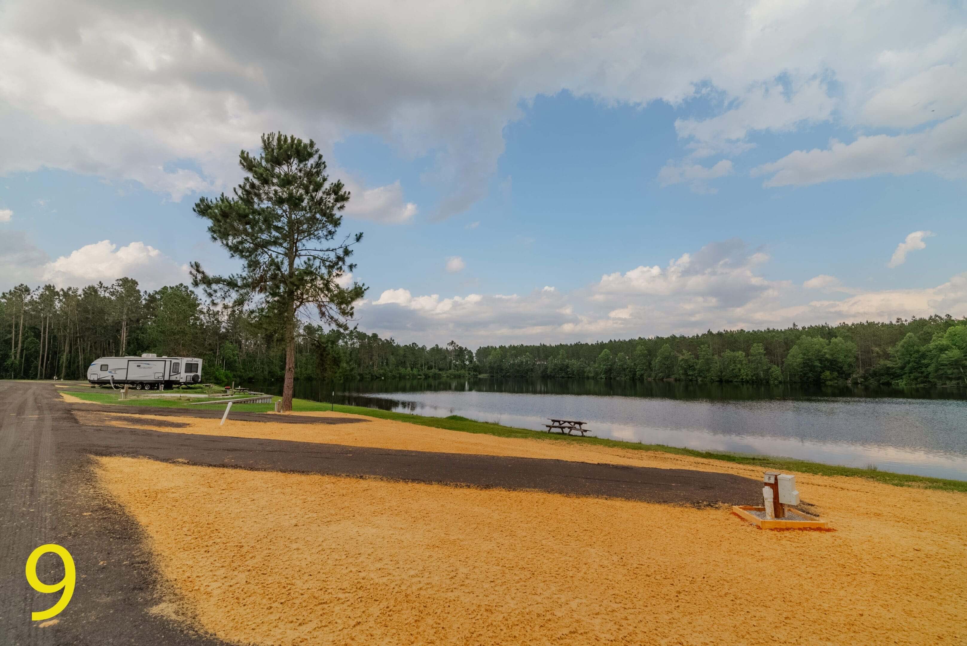 A scenic lakeside view with a tree and cloudy sky.