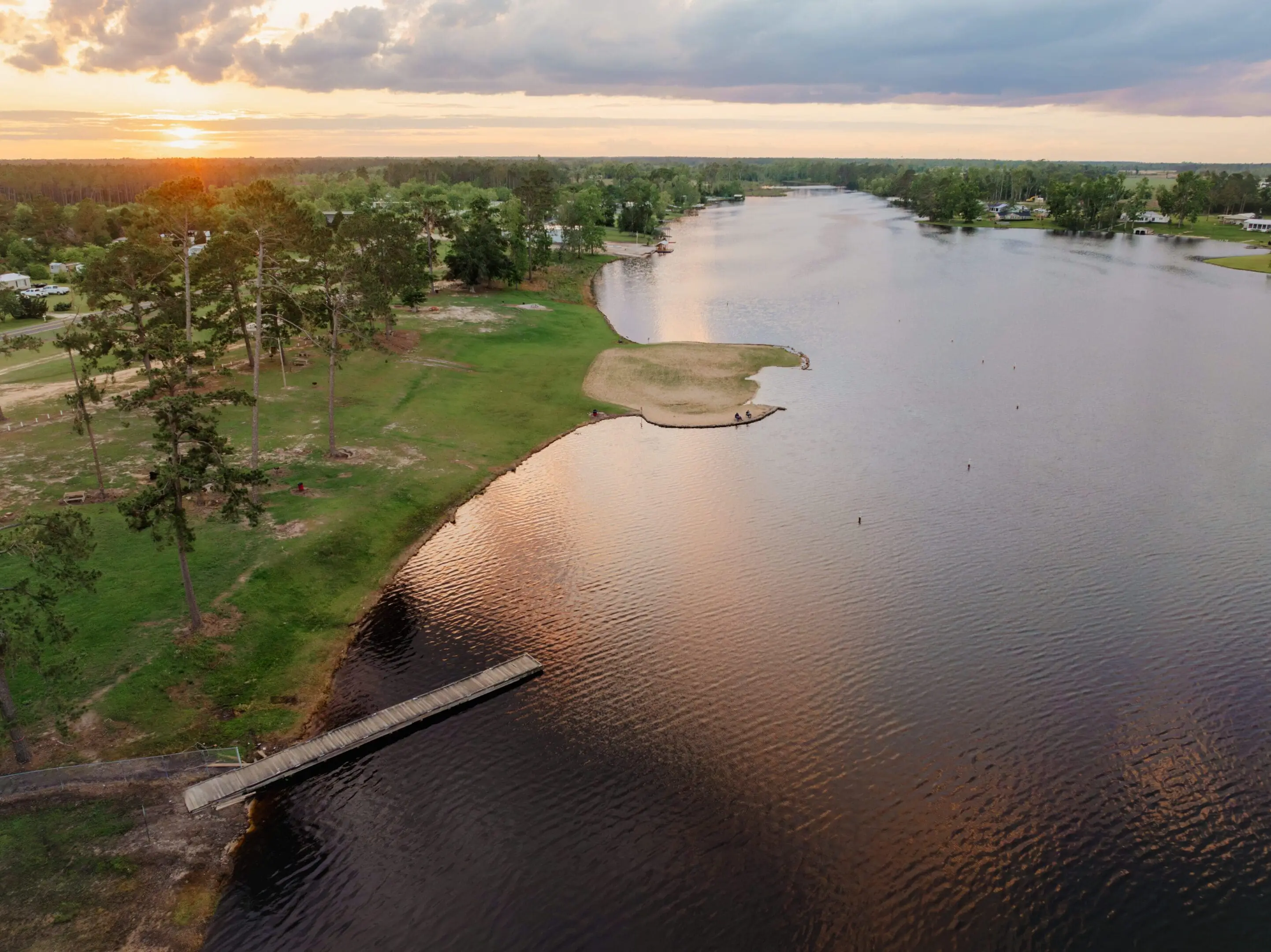 A calm river with a wooden dock at sunset.
